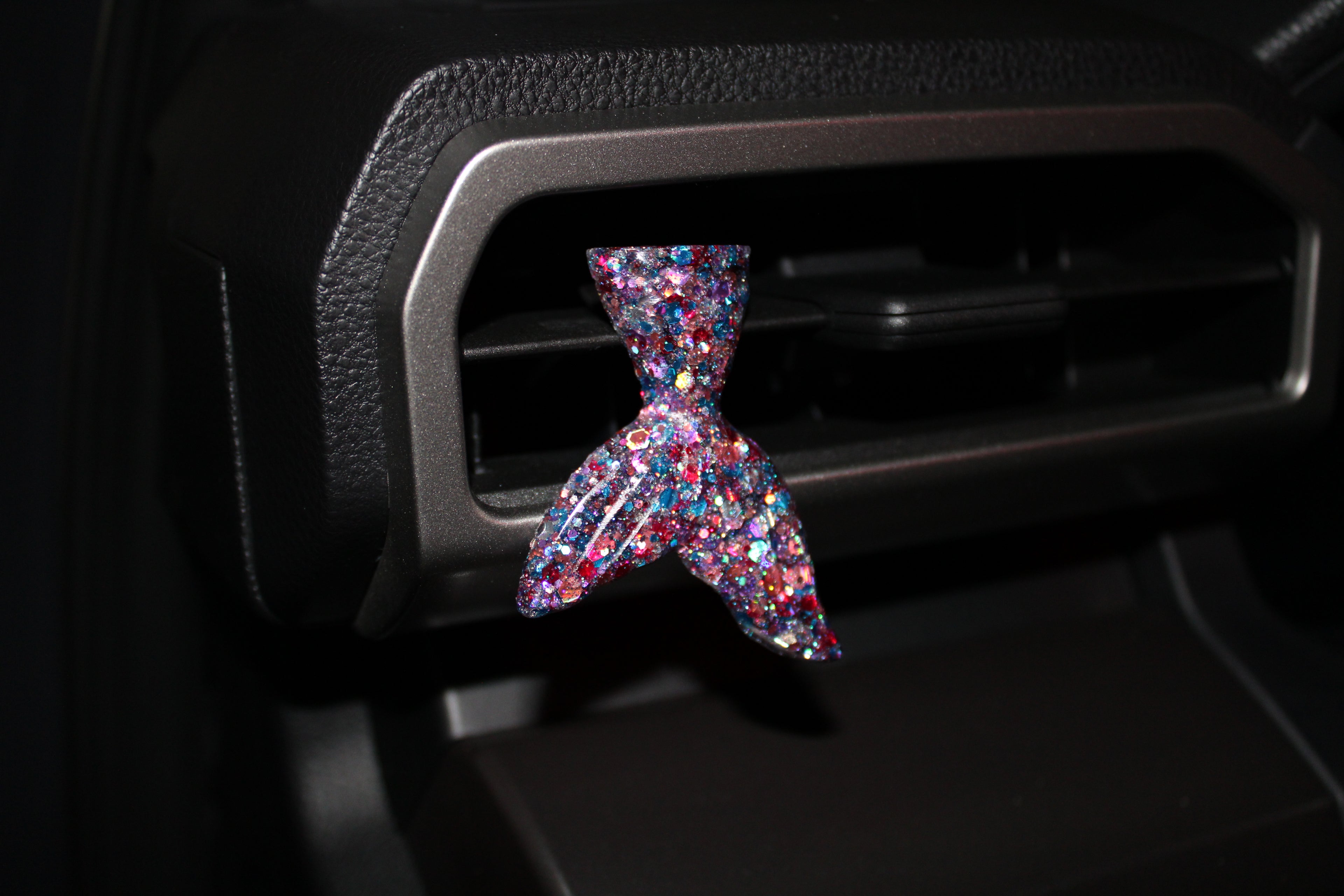 Multicolored car vent clip shaped like a mermaid tail on a car vent.