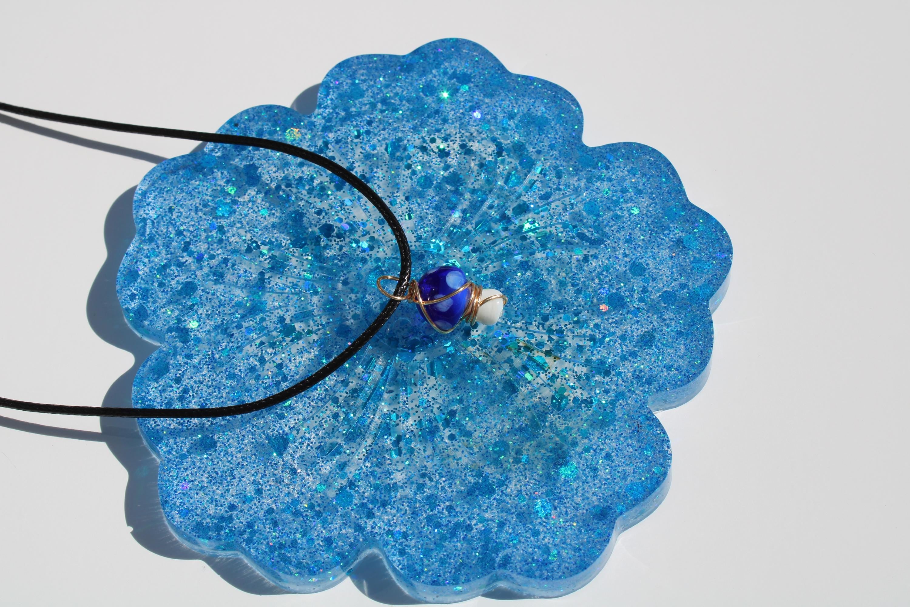 A mushroom beaded pendant necklace rests on a sparkling blue resin coaster.