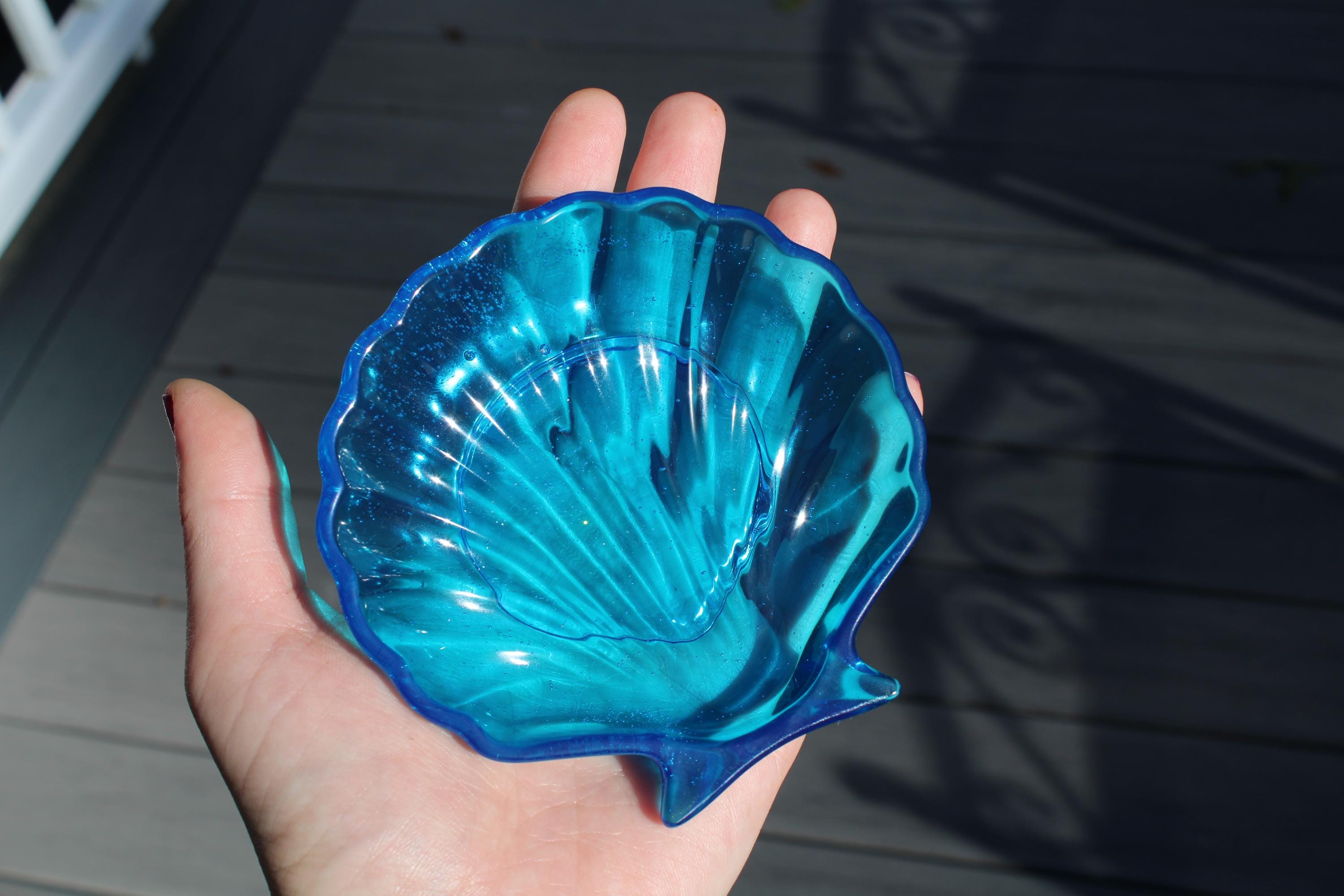 Hand holding a blue shell-shaped dish on a wooden deck