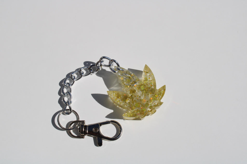 A golden resin marijuana leaf keychain with glitter sparkles on a white background.