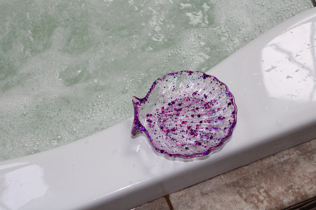 Decorative purple shell-shaped soap dish on a bathtub with water