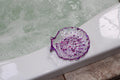 Decorative purple shell-shaped soap dish on a bathtub with water