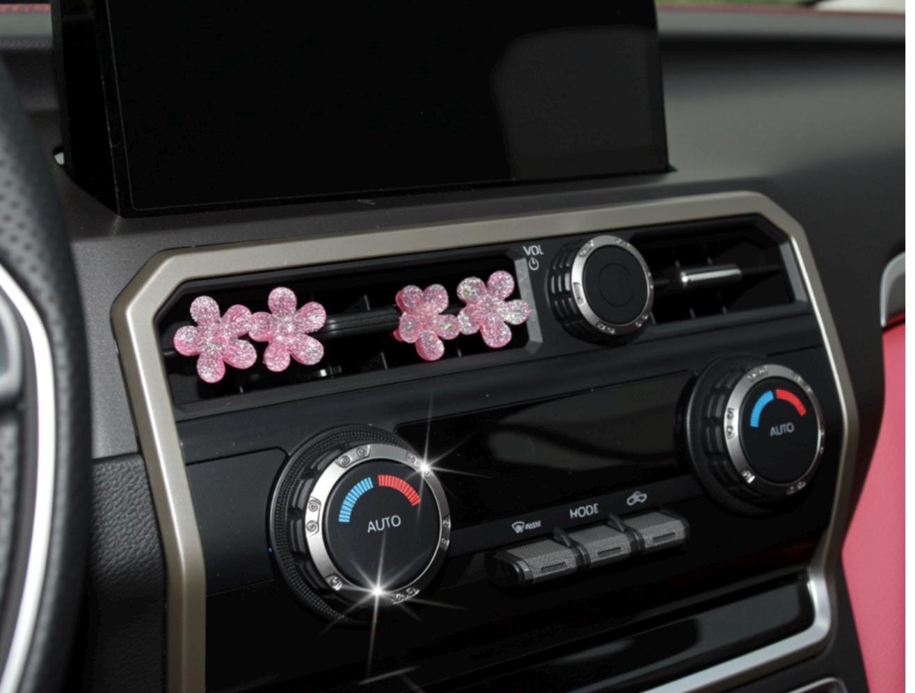 Car air vent with decorative pink flowers and control knobs.
