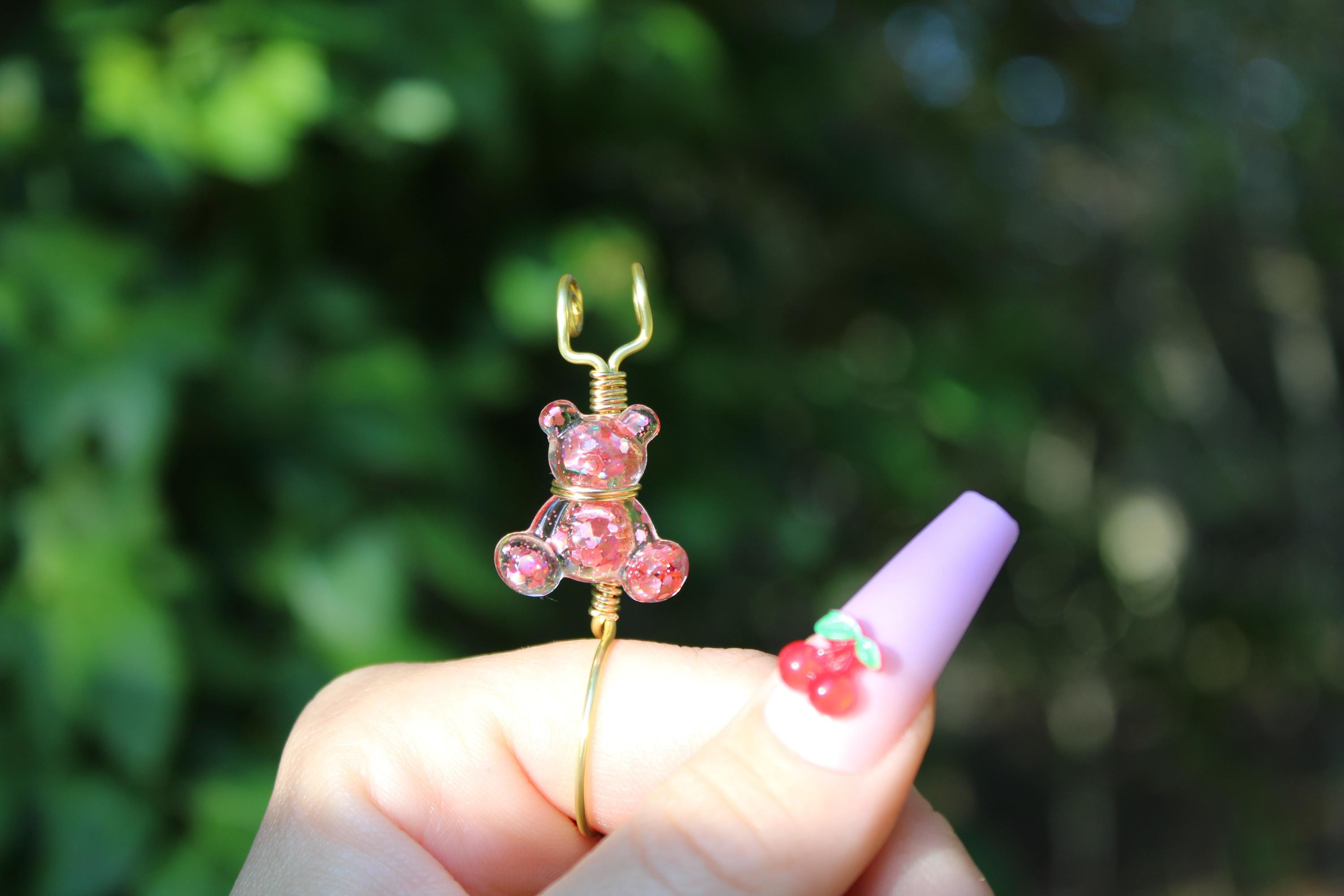 A hand displays a pink sequin teddy bear smoke ring in front of a leafy background.