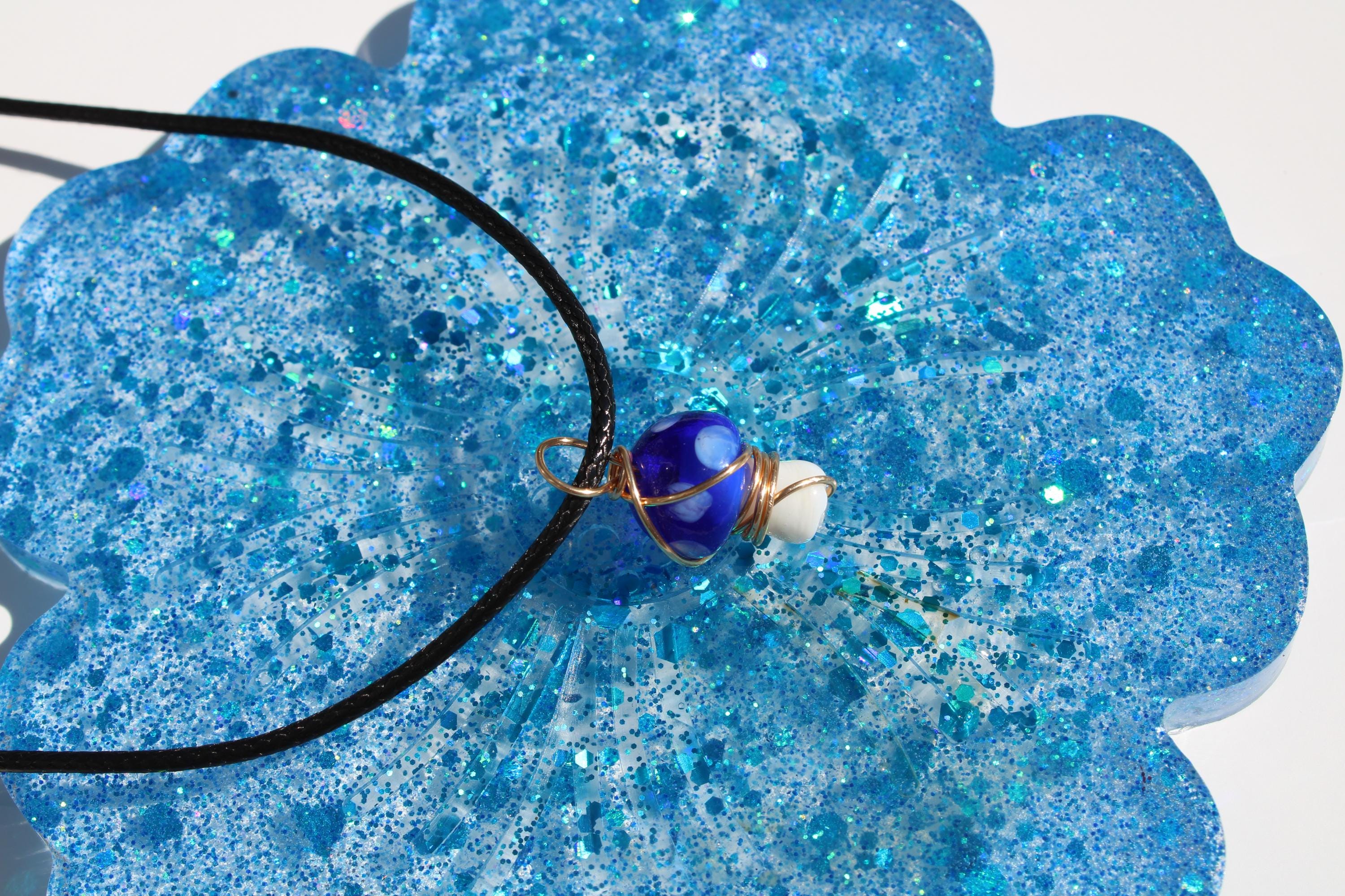 Handmade blue glitter resin coaster displays a unique glass bead mushroom pendant necklace.