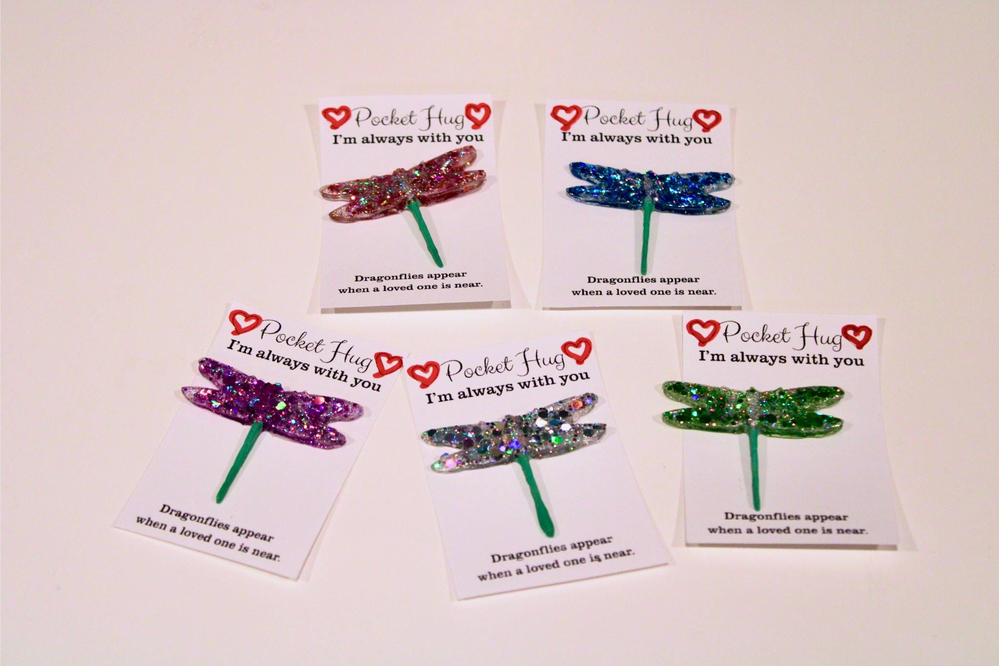 Five dragonfly-shaped charms on cards with text on a beige background