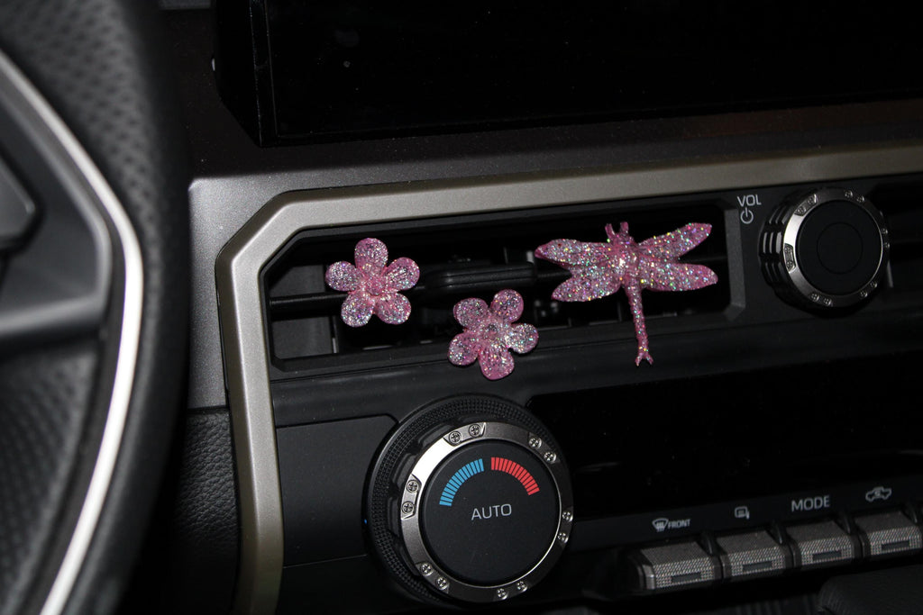 Decorative car decor shaped like flowers and a dragonfly on a car dashboard.