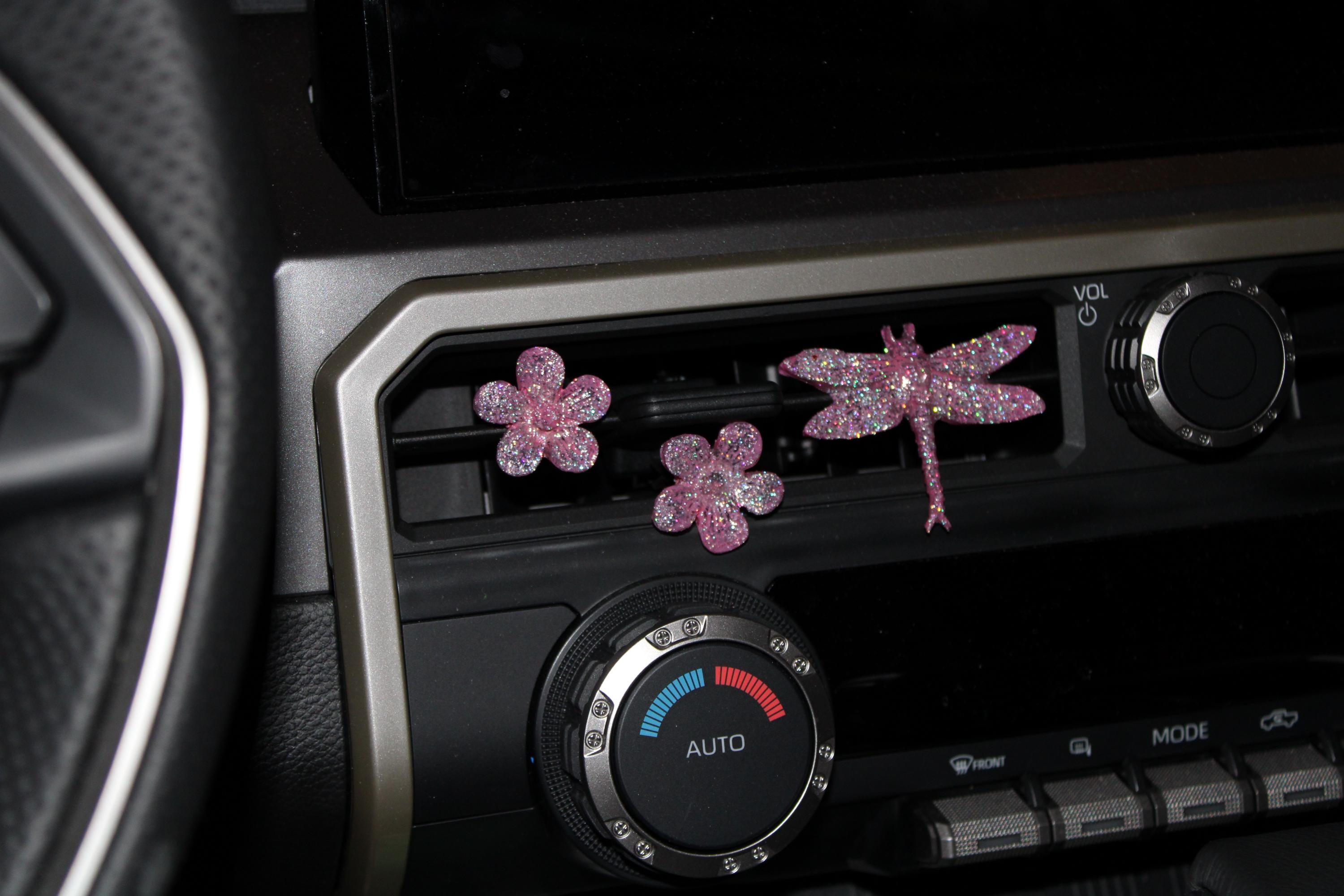 Decorative car decor shaped like flowers and a dragonfly on a car dashboard.