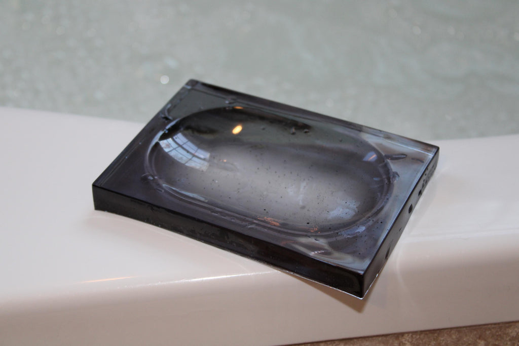 A smokey resin soap dish rests on the edge of a white bathtub.