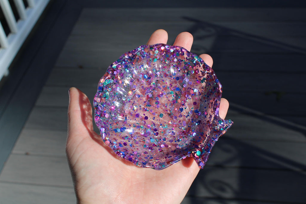 Hand holding a glittery purple shell-shaped object against a neutral background