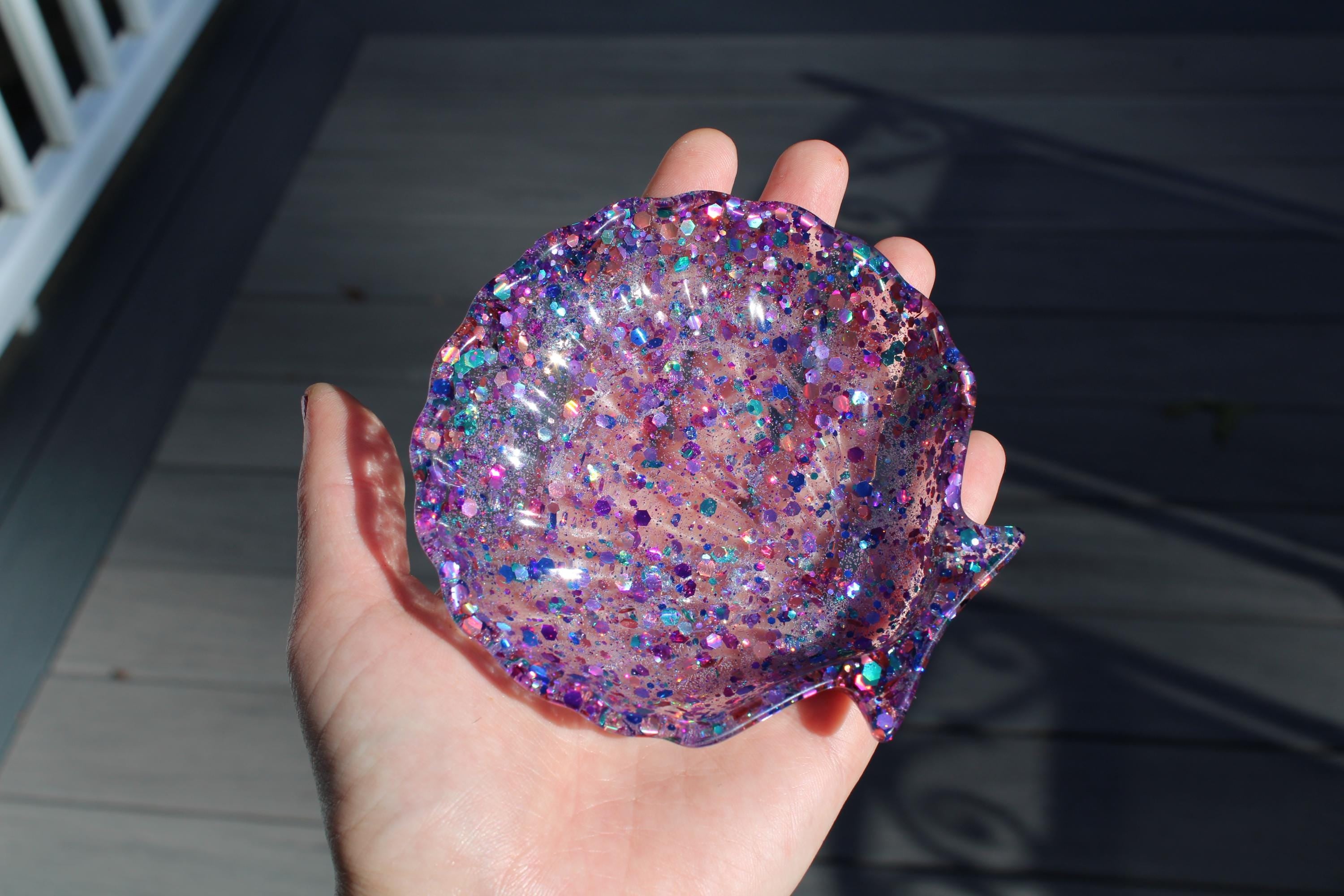 Hand holding a glittery purple shell-shaped object against a neutral background