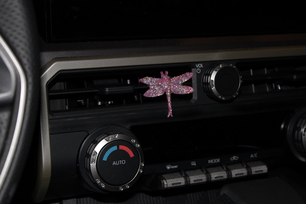 Car air vent with decorative pink dragonfly sticker on a dark background