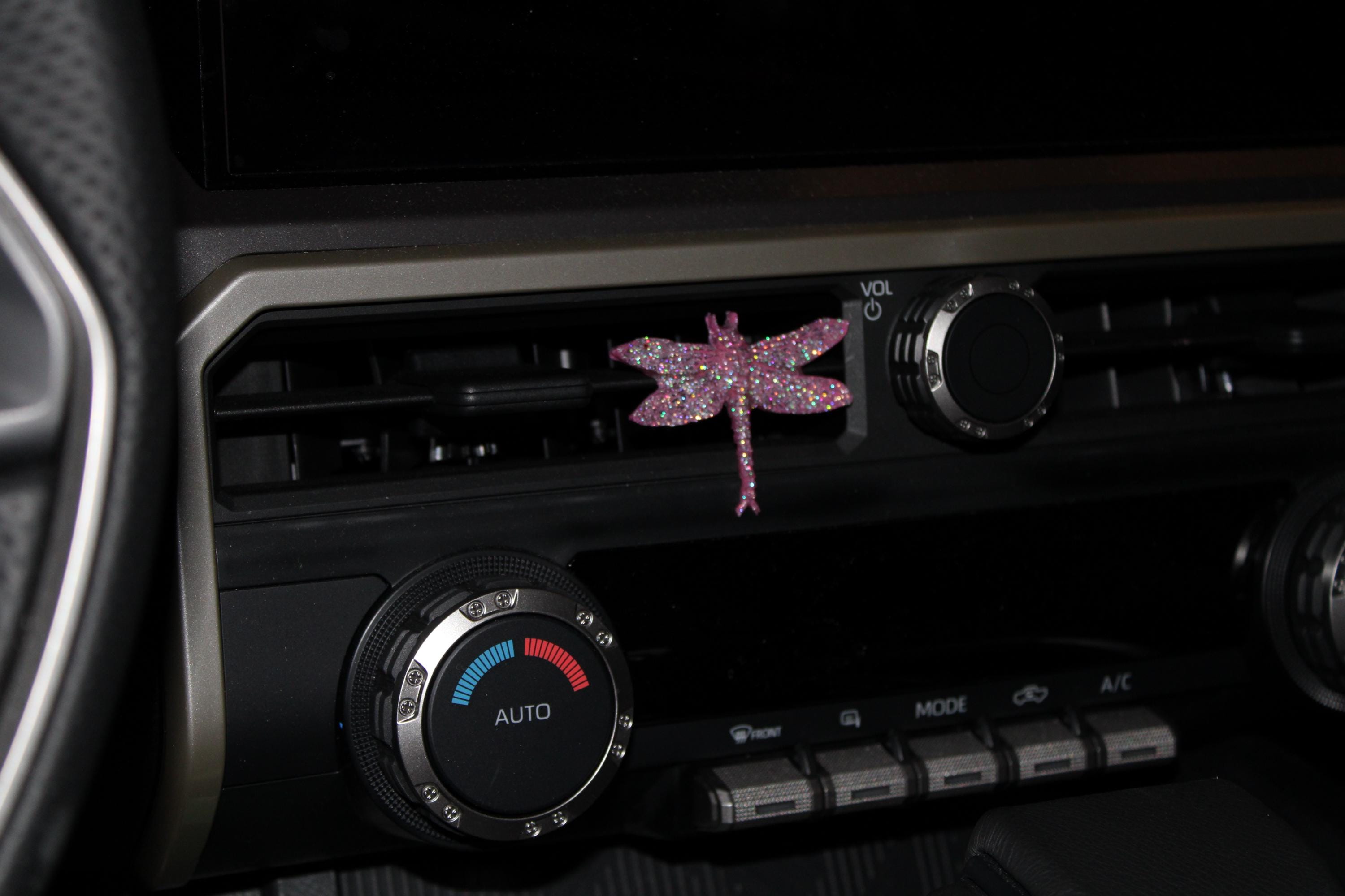Car air vent with decorative pink dragonfly sticker on a dark background