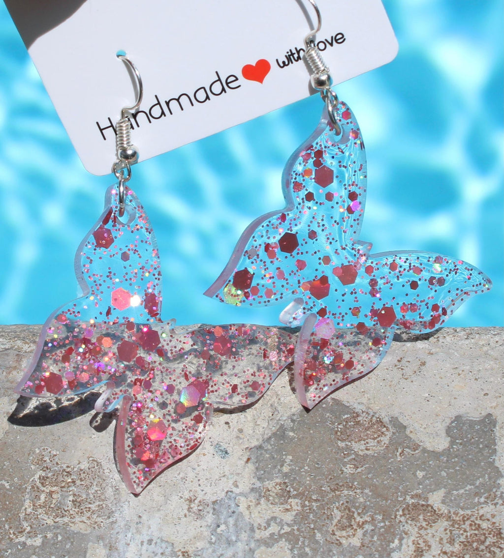 Butterfly-shaped earrings with glittery design on a blue and gray background