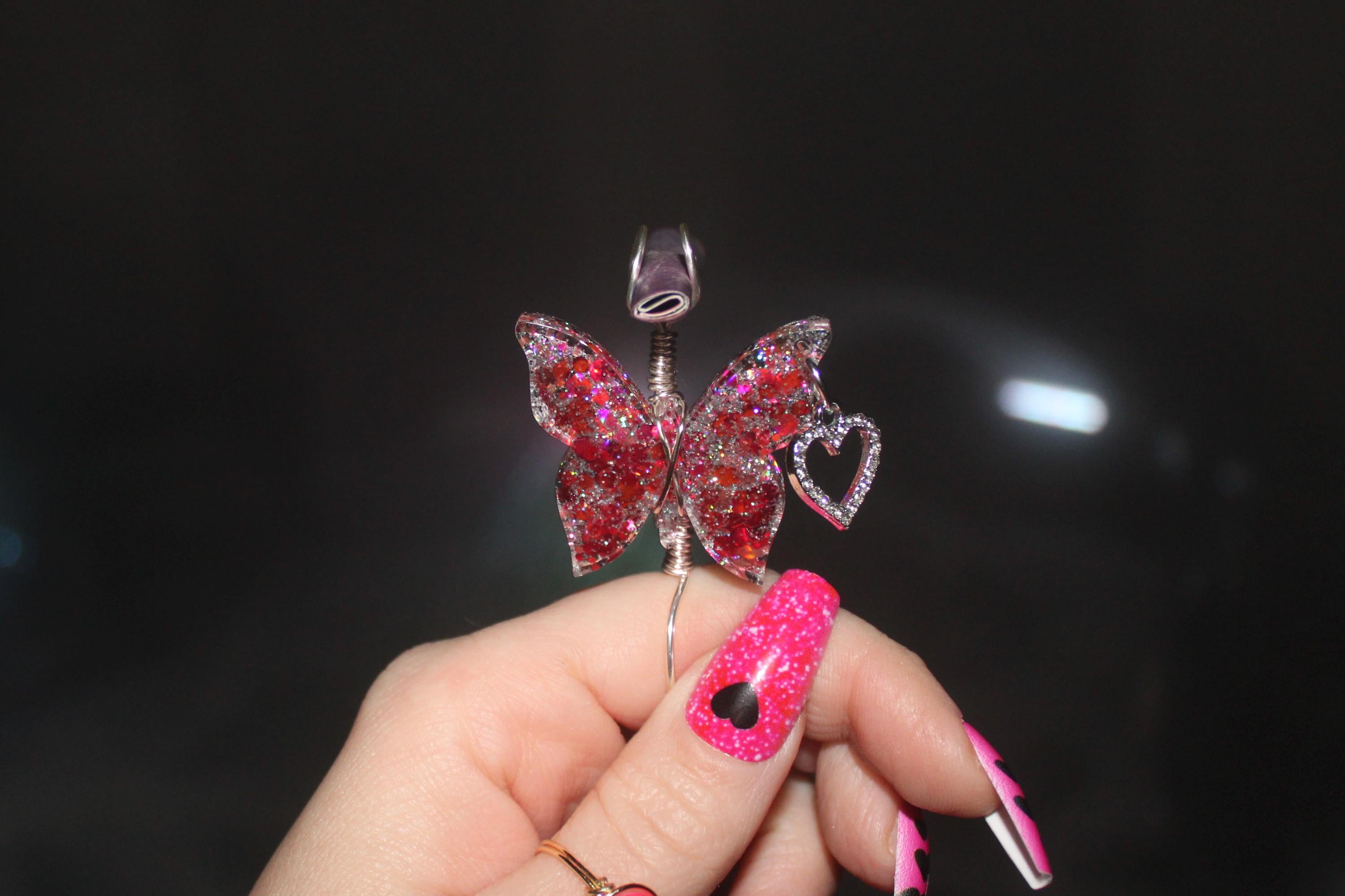 Butterfly-shaped smoke ring with pink gemstones held by a hand against a dark background