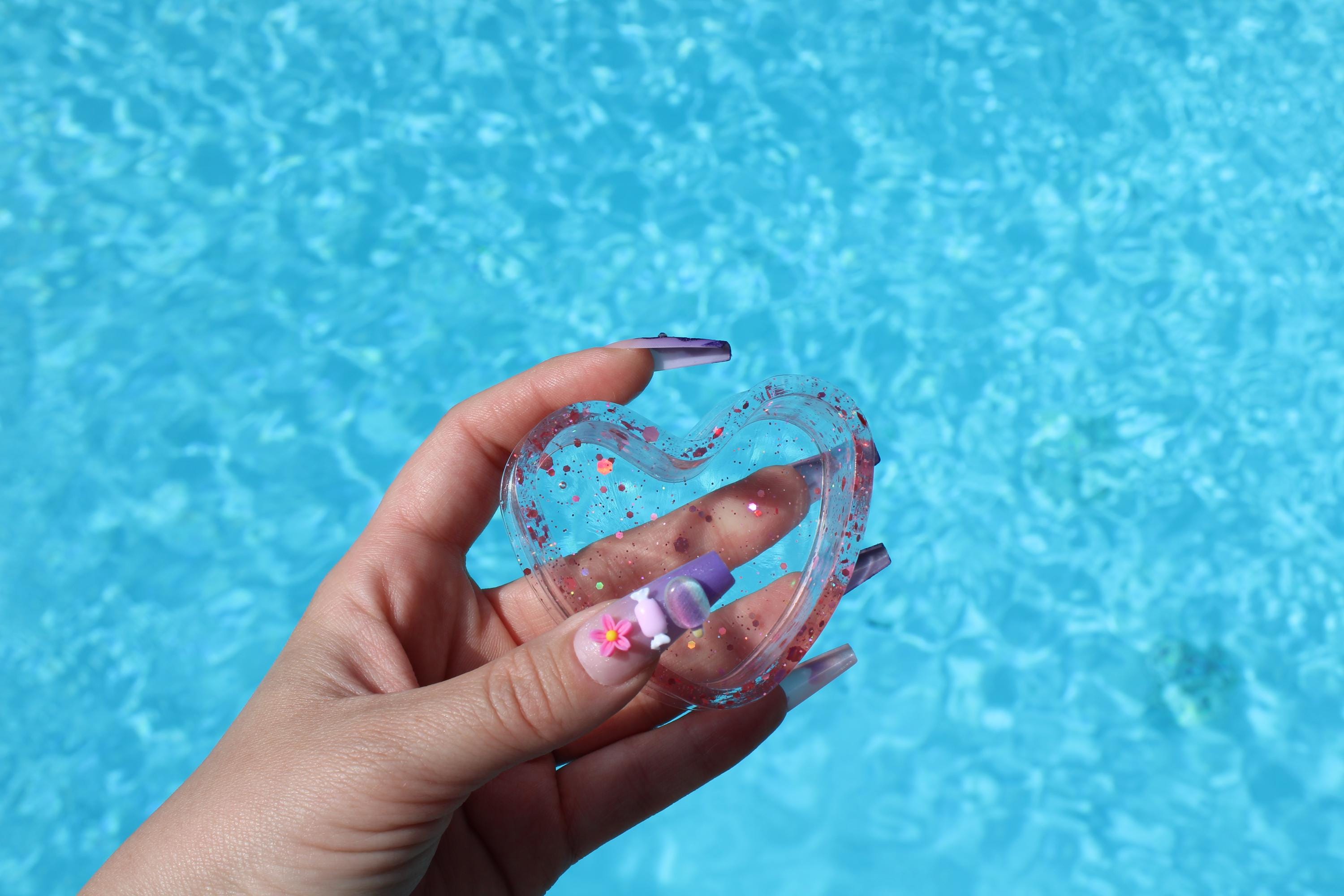 Heart-shaped clear dish with pink heart design held by a hand against a blue water background