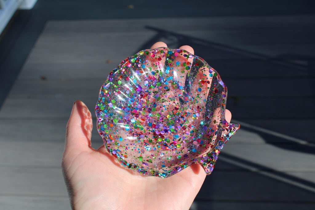 Hand holding a glittery, multicolored shell-shaped object against a dark background