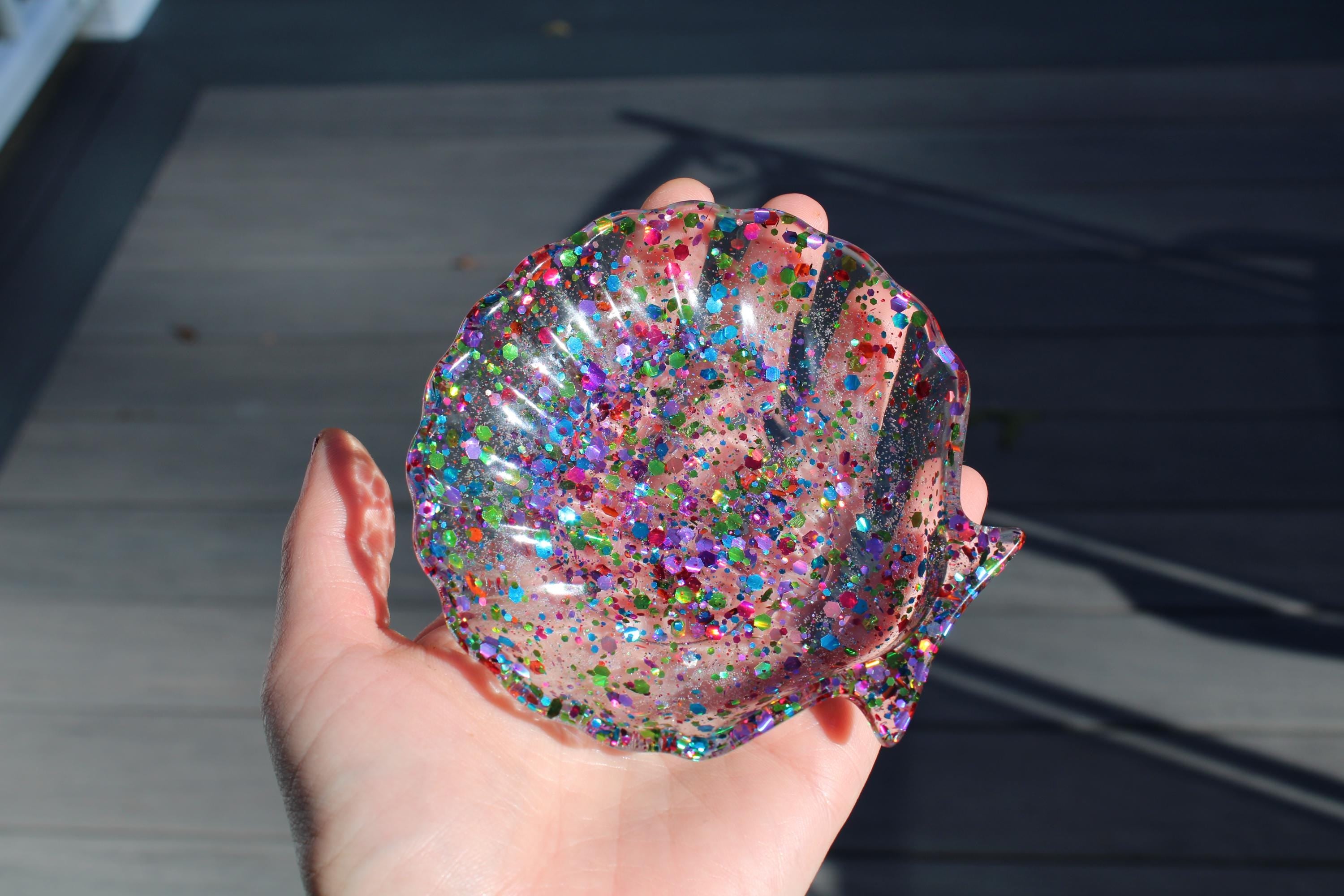 Hand holding a glittery, multicolored shell-shaped object against a dark background