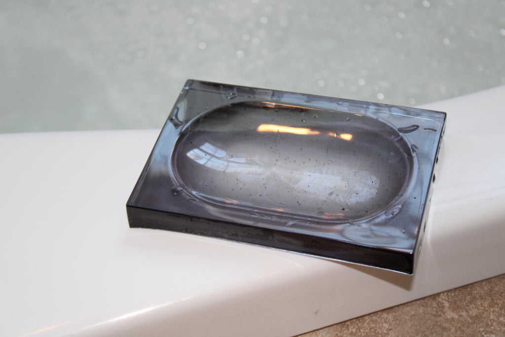 A black resin soap dish rests on the edge of a white bathtub during a relaxing bath.