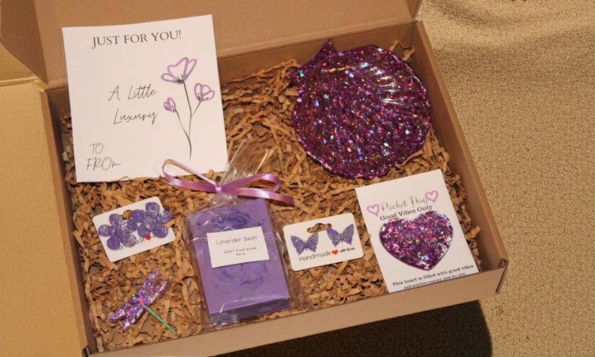 Gift box with purple items including a soap, card, and decorative elements on a beige surface.