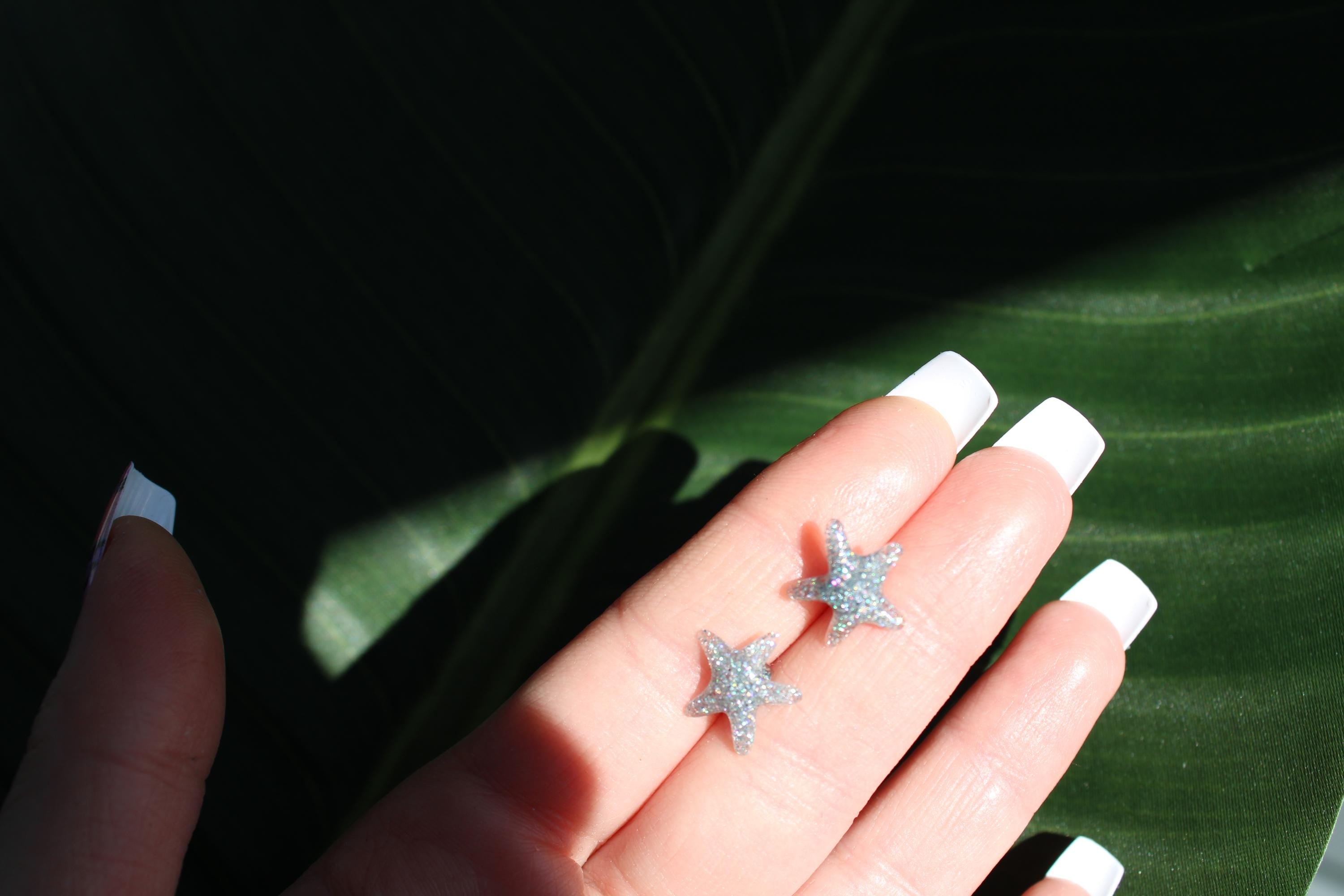 Star-shaped earrings on a hand with a green leaf background