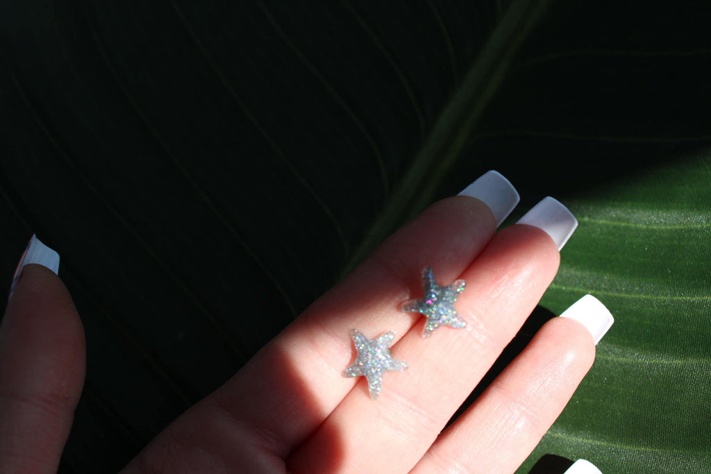 Star-shaped earrings held between fingers against a dark background
