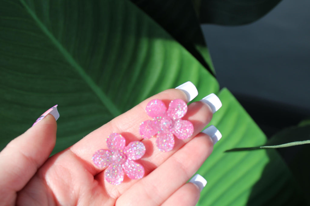 Pink glittery flower-shaped objects held in a hand with a green leaf background