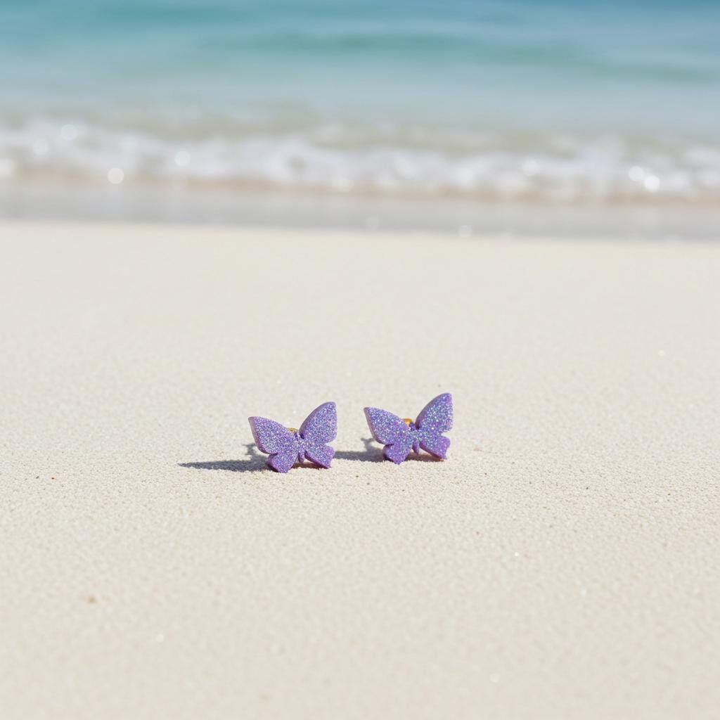 Purple butterfly earrings on a sandy beach with ocean in the background