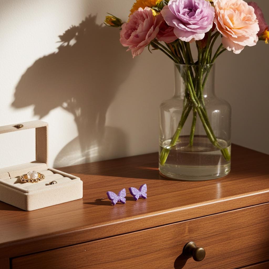Butterfly-shaped earrings on a wooden surface with a vase of flowers and jewelry box in the background.