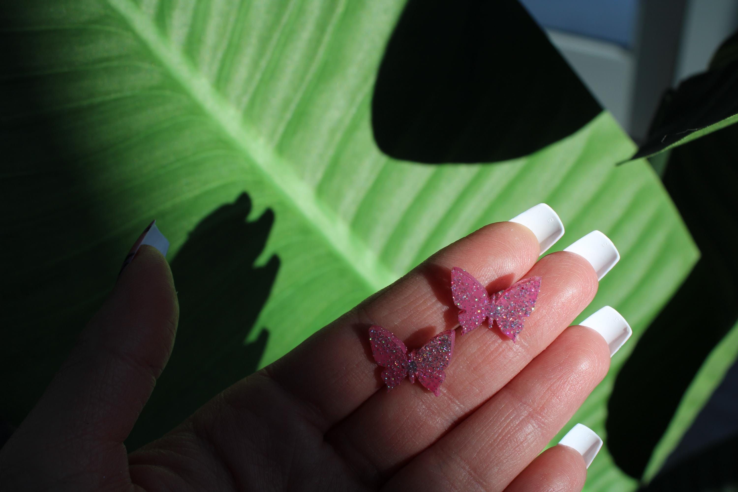 Hand holding pink butterfly-shaped candies with a green leafy background