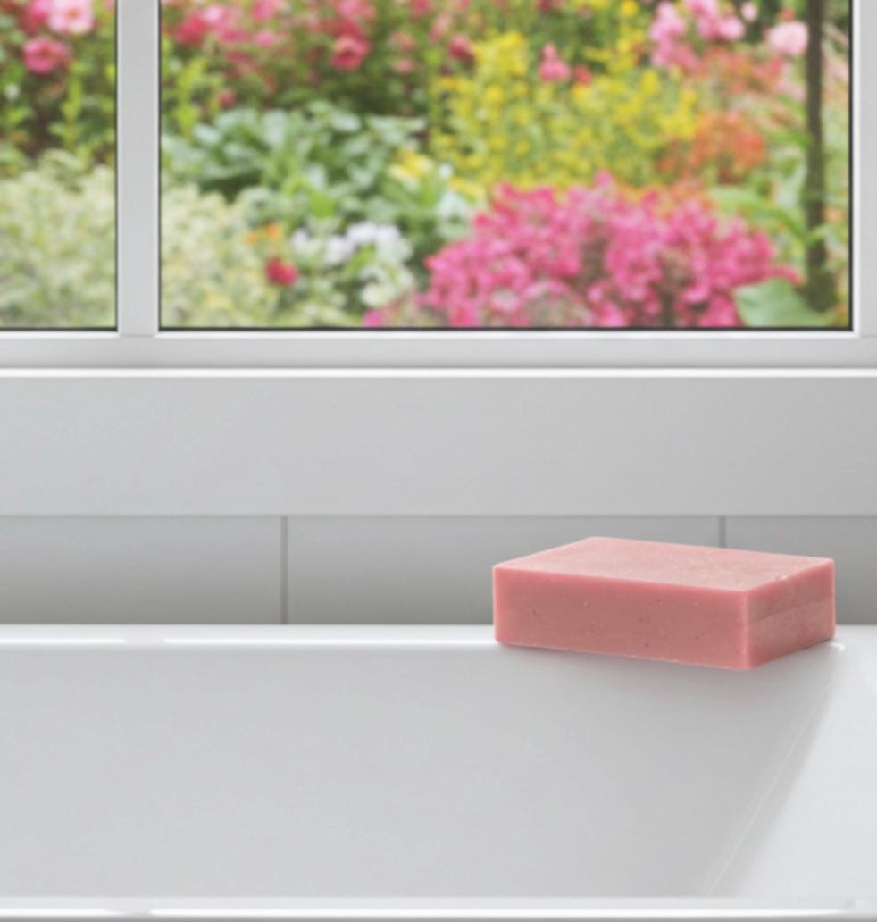 Pink soap bar on a white surface with a window showing a garden view