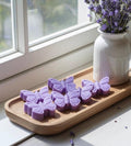 Butterfly-shaped purple soap bars on a wooden tray with a vase of lavender in the background.