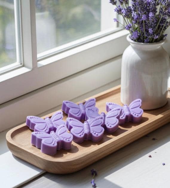 Butterfly-shaped purple soap bars on a wooden tray with a vase of lavender in the background.