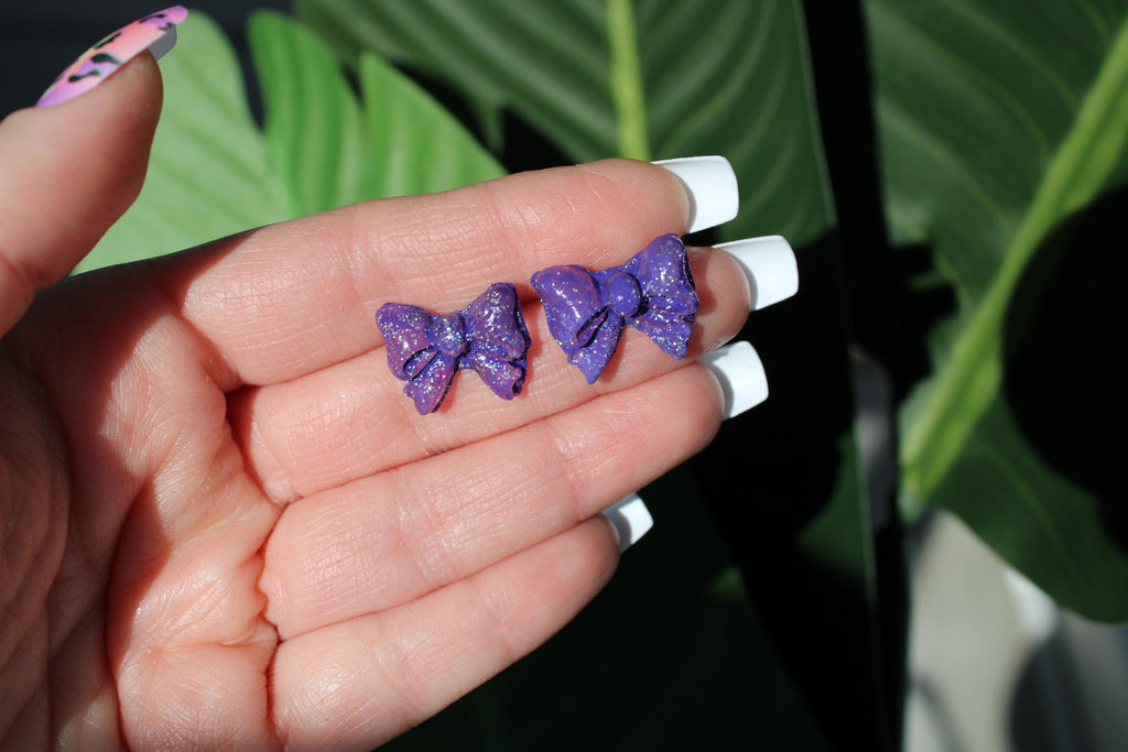 Hand holding two purple glittery bow-shaped objects against a green leafy background