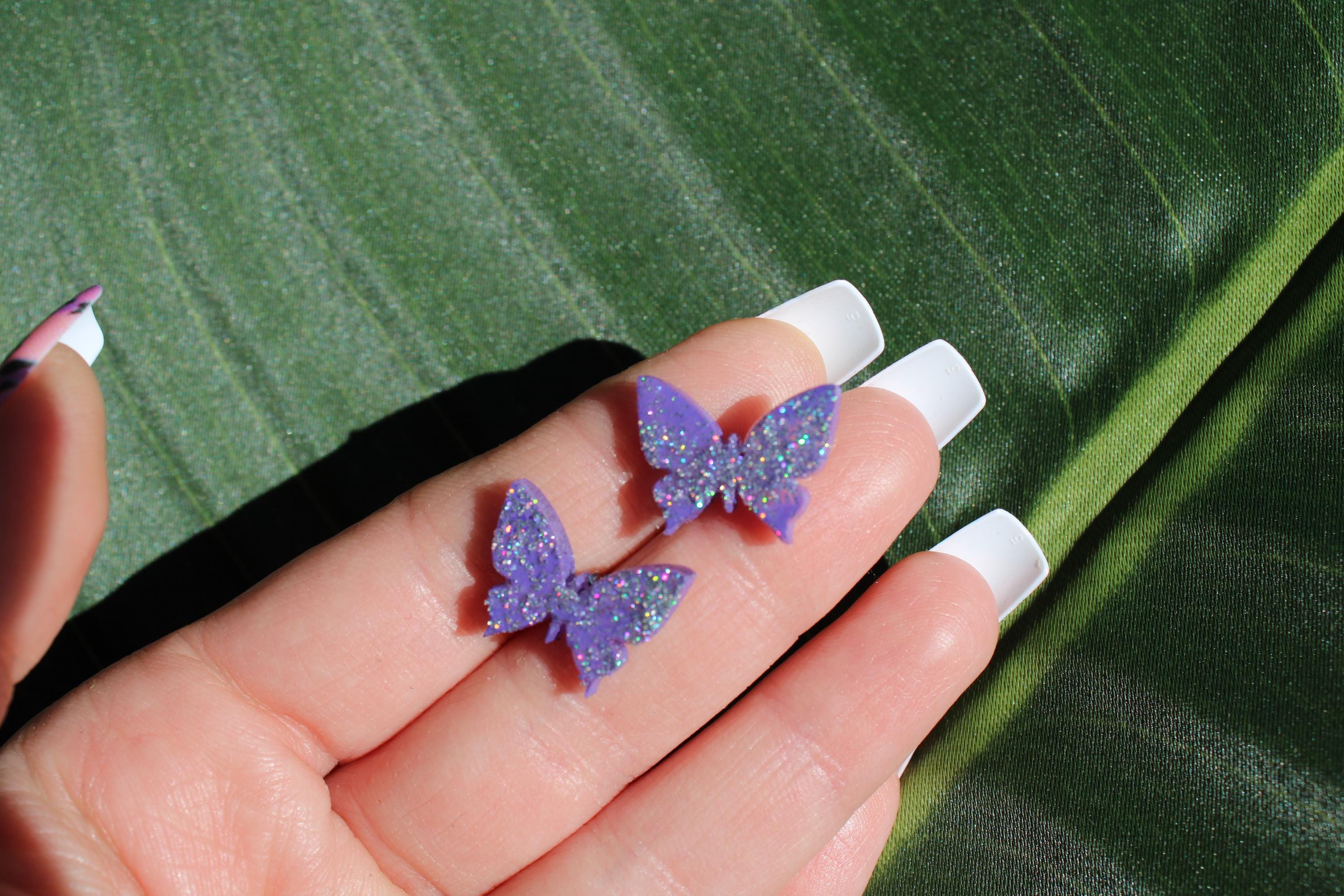 Purple butterfly earrings held in a hand with a green leaf background