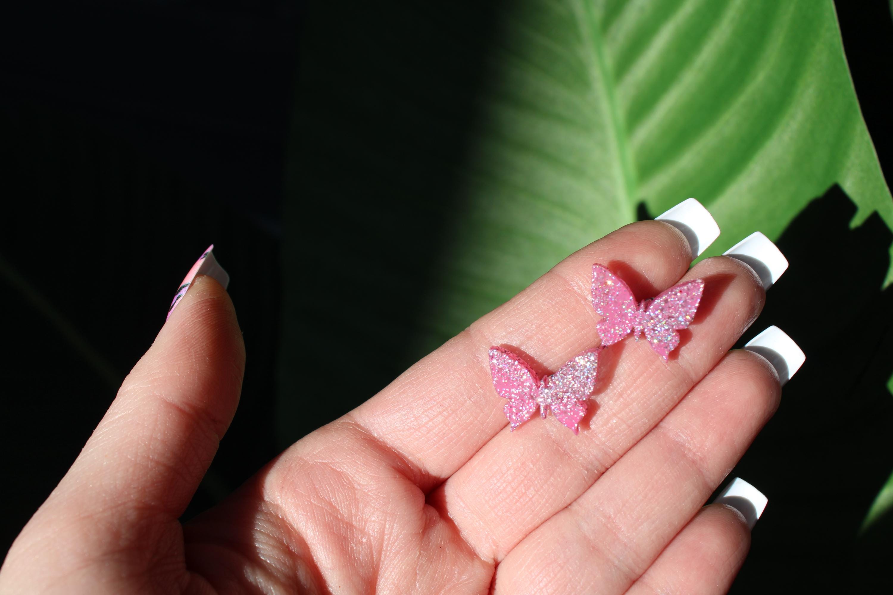 Pink butterfly earrings held in a hand with a green leaf background