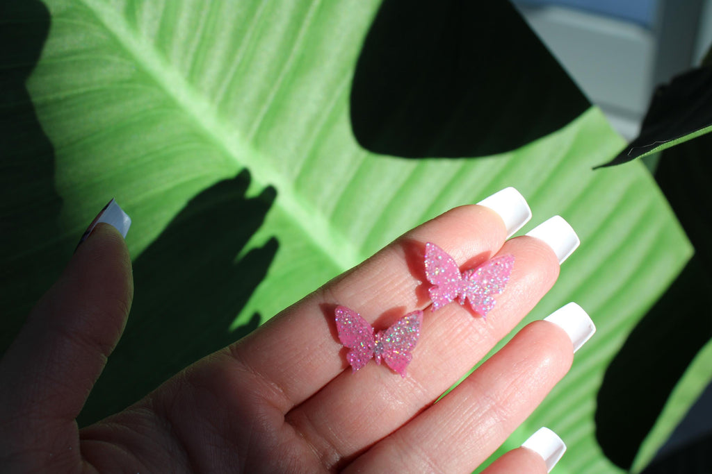 Hand with pink glittery butterfly decorations on a green leaf background