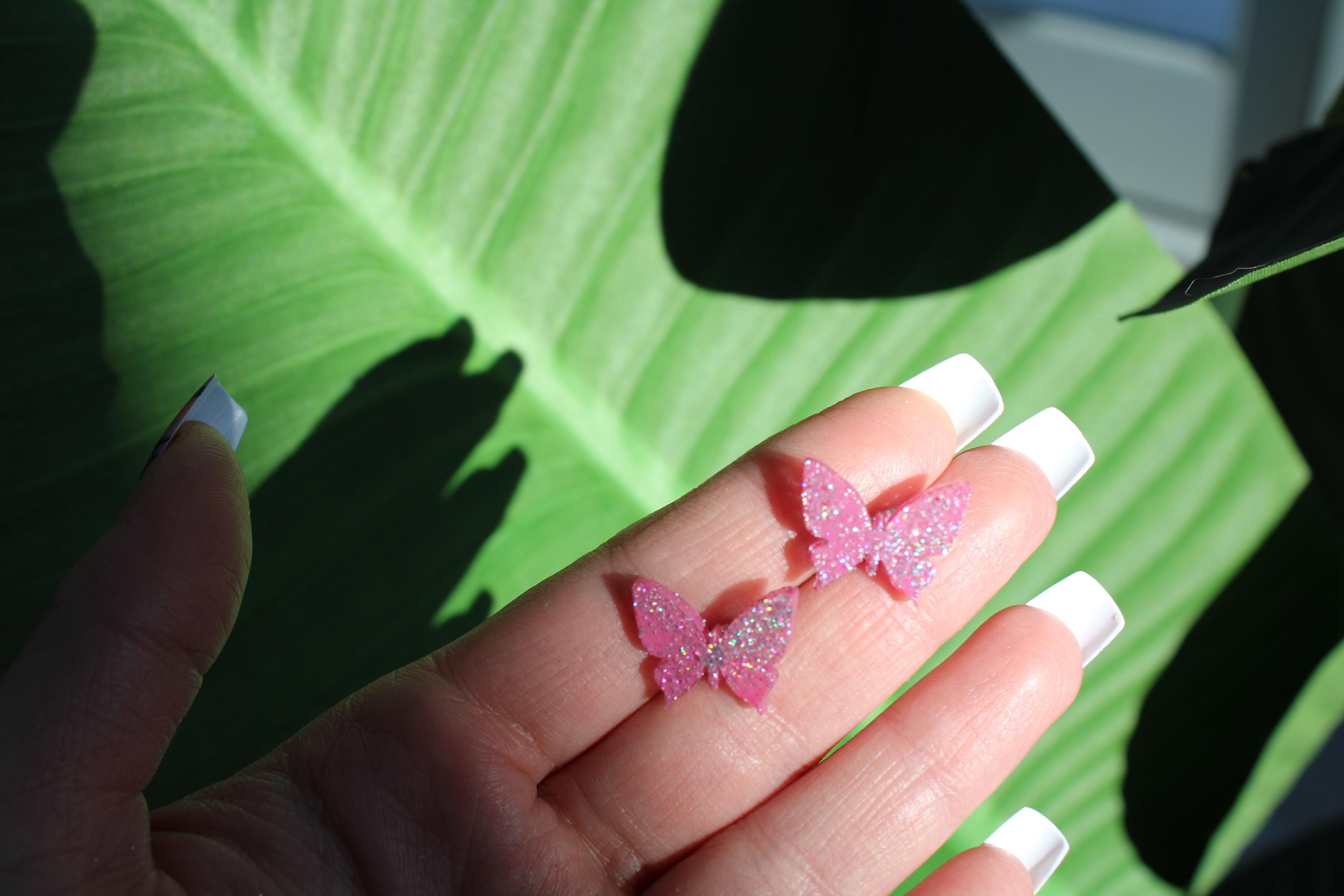 Hand with pink glittery butterfly decorations on a green leaf background