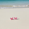 Pink butterfly earrings on a sandy beach with ocean waves in the background