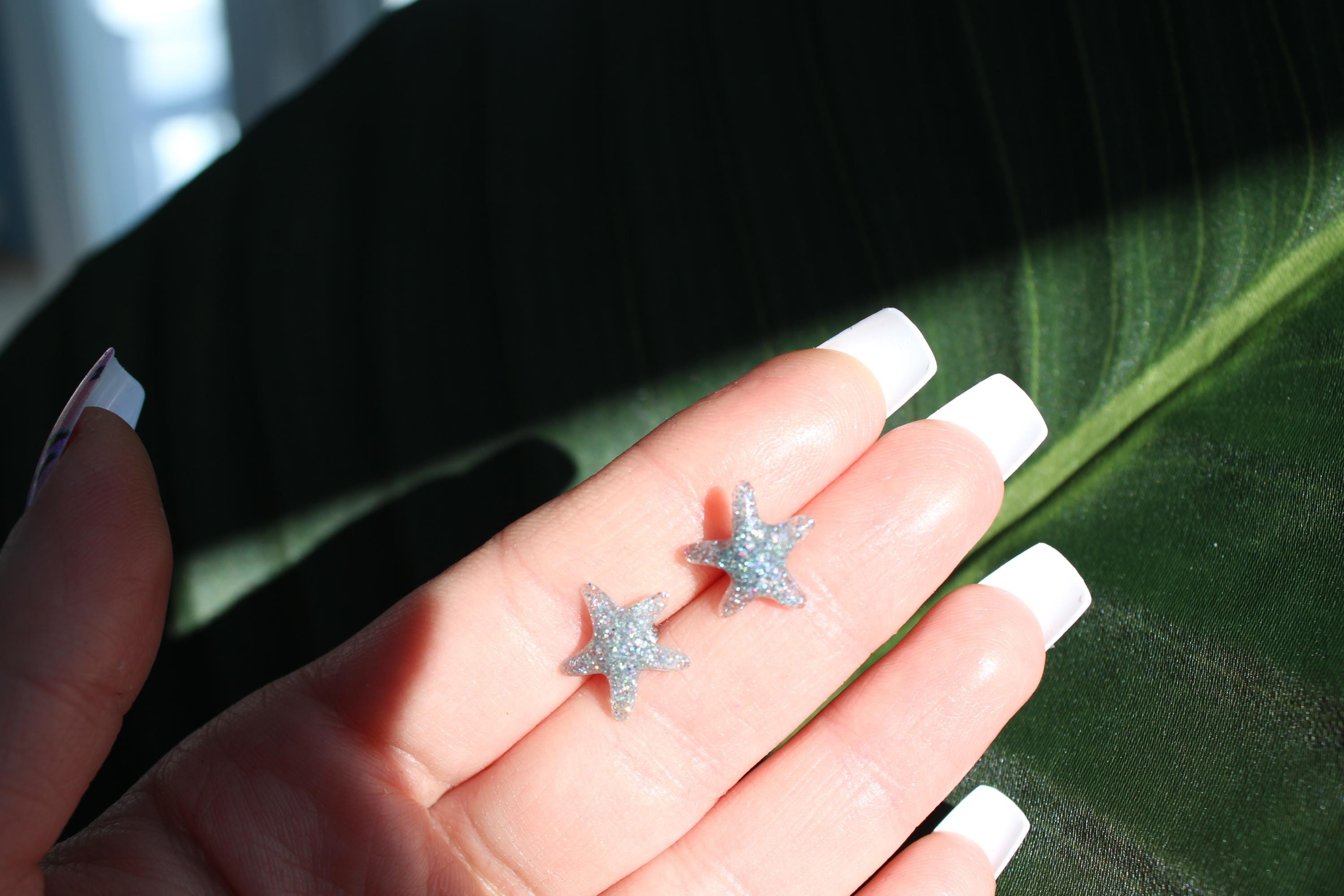 Star-shaped earrings held between fingers against a dark background