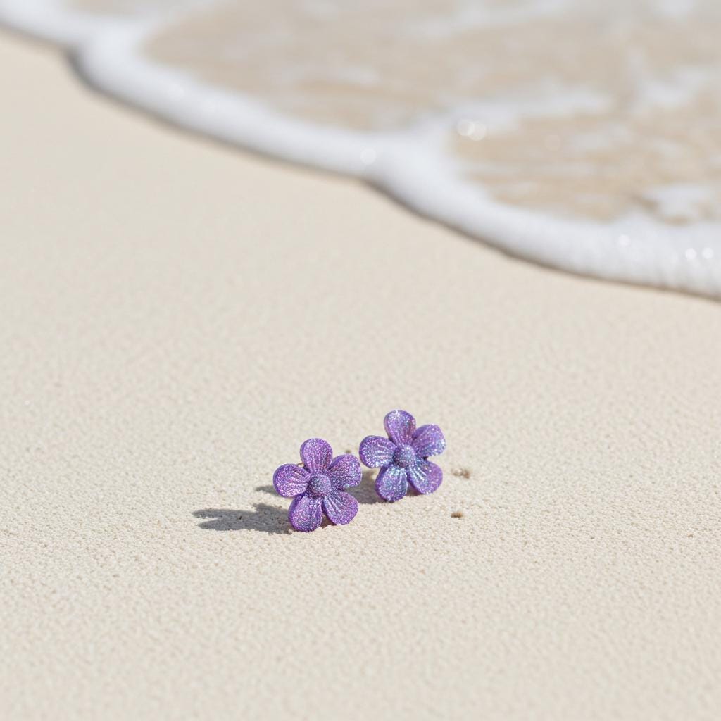 Purple flower earrings on a sandy beach with waves in the background