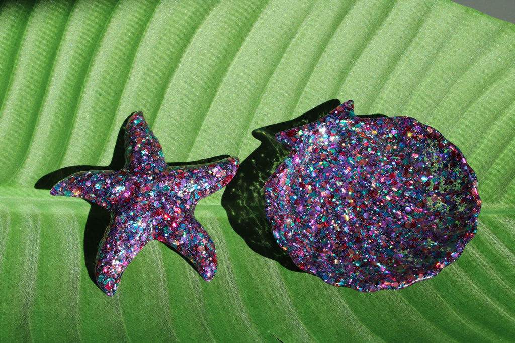 Glittery starfish and seashell dish on a green leaf background