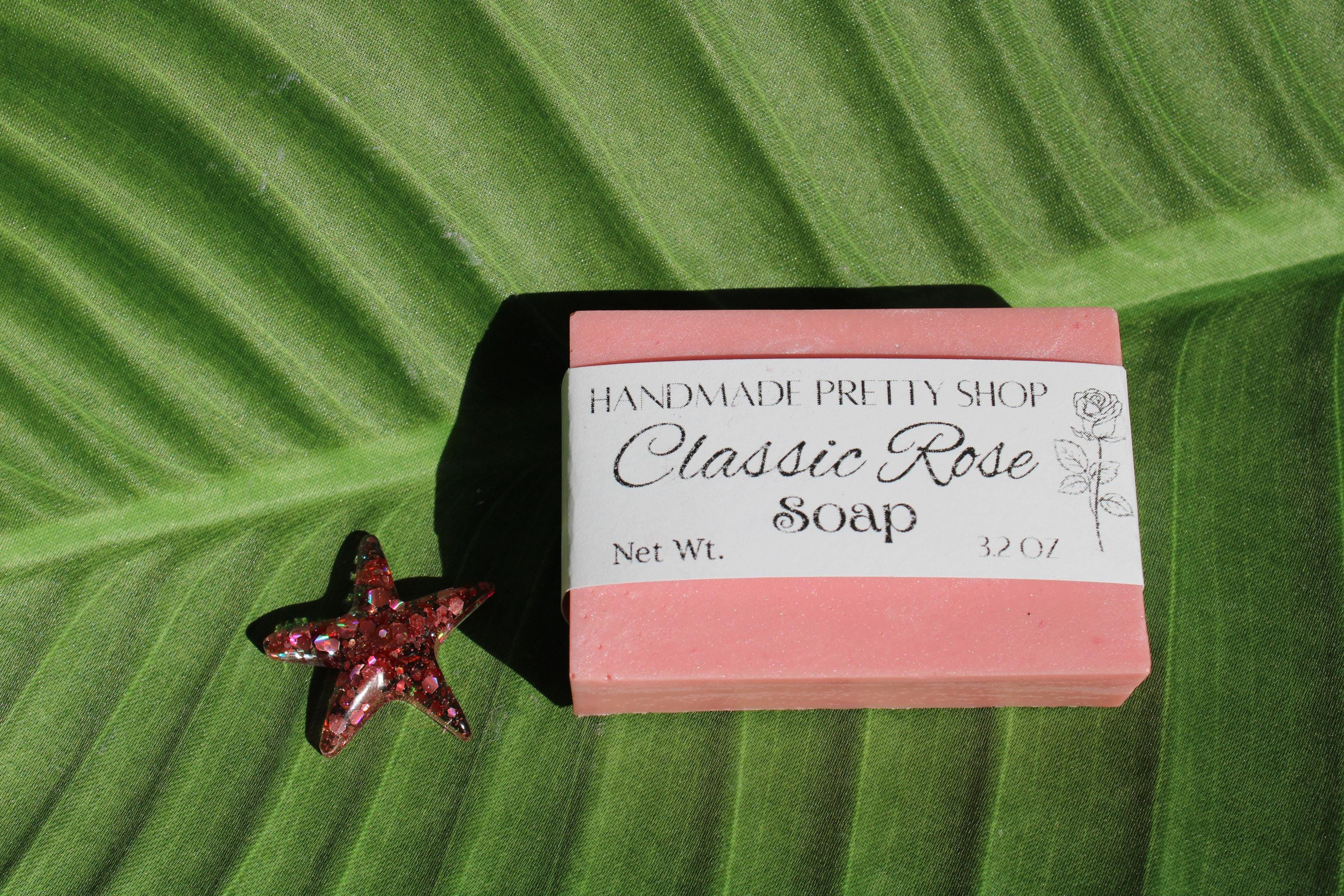 Bar of soap labeled 'Classic Rose Soap' from 'Handmade Pretty Shop' on a green leaf with a red starfish.