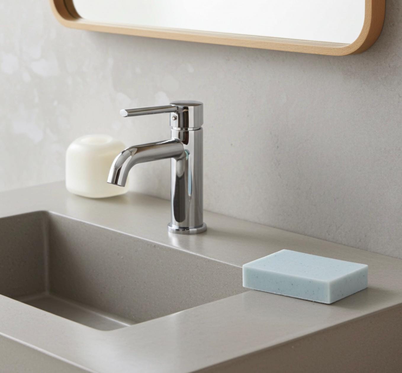 Modern bathroom sink with faucet, soap, and sponge on a neutral countertop.