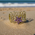Gold bracelet with a purple starfish charm on a sandy beach