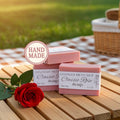 Handmade soap bars with a red rose on a wooden table outdoors.