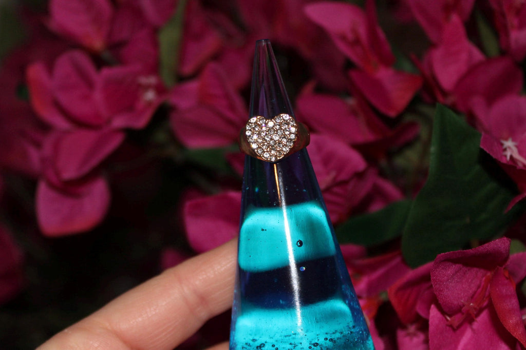 Ring with a heart-shaped diamond on a blue ring display against a pink flower background