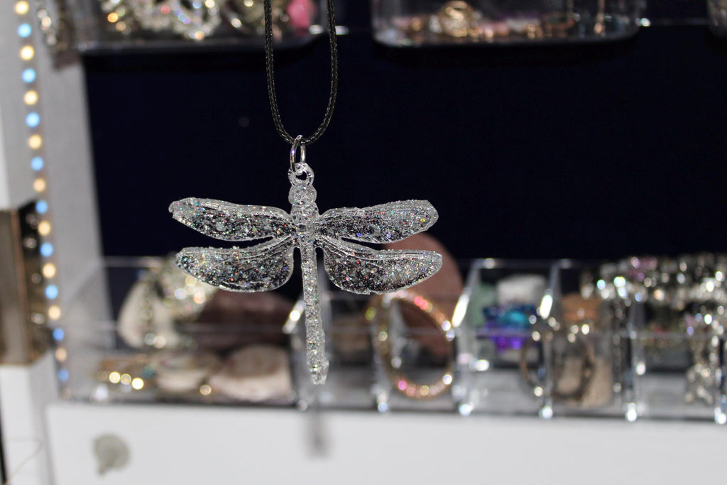 Silver dragonfly-shaped pendant on a chain against a blurred jewelry store background.