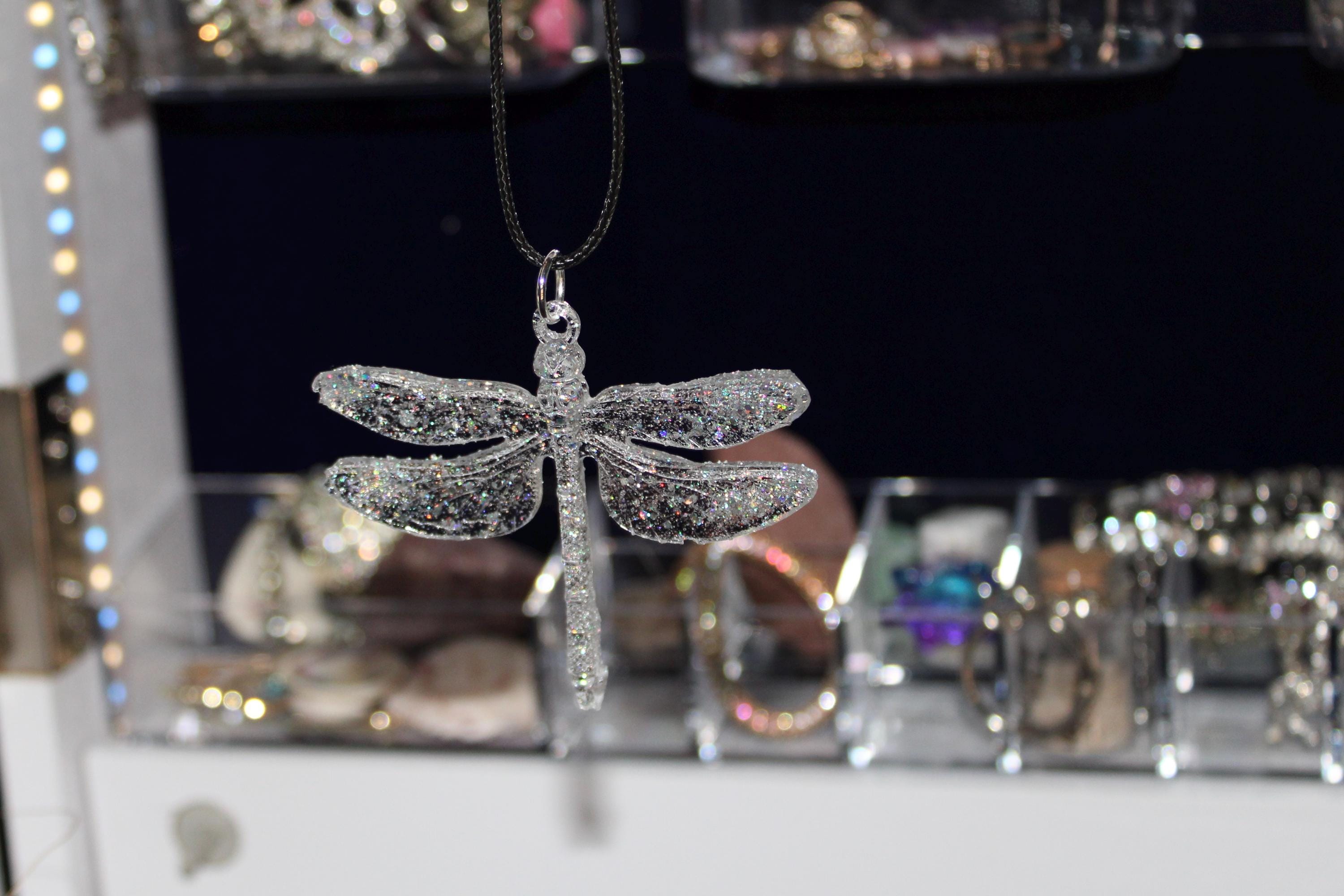 Silver dragonfly-shaped pendant on a chain against a blurred jewelry store background.