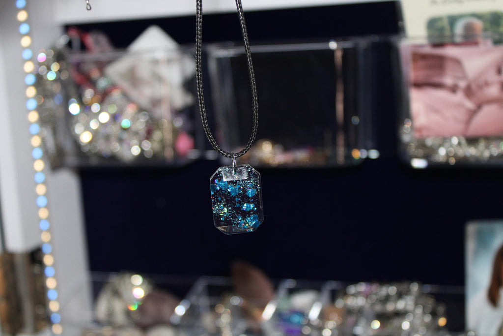 Necklace with a blue crystal pendant in front of a blurred jewelry store display.